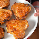 A white plate holds several pieces of crispy, golden-brown cooked chicken with charred edges, each piece dusted with The Spice Lab Nom Nom Paleo Magic Mushroom Powder by The Spice Lab for an extra burst of savory umami seasoning.