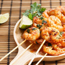 Grilled shrimp skewers with herbs are served on a wooden plate, garnished with lime wedges and fresh parsley atop a bamboo mat—elevate this dish with The Spice Lab Cooking Essentials Seasoning Set by The Spice Lab for an unforgettable flavor experience.