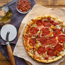Pepperoni pizza with bell peppers and herbs on parchment, served beside a pizza cutter, The Spice Lab Organic Crushed Red Pepper Flakes, and a bottle of oil—set on a wooden table with a cloth napkin—for a delicious blend perfect for fans of authentic Italian cooking.