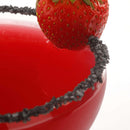 A close-up of a red cocktail in a glass with a rim coated in The Spice Lab Black Obsidian Salt Cocktail Rimmer by The Spice Lab, garnished with a fresh strawberry on the edge.