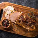 Sliced roast beef on a wooden cutting board with herbs and The Spice Lab Kings Blend Peppercorn Grinder Refill, shot from above on a dark surface.