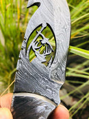 A close-up of the Texan Knives Deer Knives – 10" wire-cut Damascus steel blade with antler horn handle and leather sheath, shown outdoors against blurred green grass.