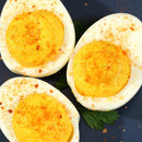 Three deviled eggs on a dark plate, topped with a sprinkle of paprika and garnished with a green herb leaf underneath, offering a savory flavor enhanced by The Spice Lab Slow Burn Seasoning from The Spice Lab.