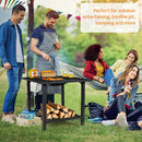 Four friends relax outside—one grills on the 31 Inch Outdoor Fire Pit Dining Table with Cooking BBQ Grate by DirectDeals, while others enjoy snacks and drinks nearby. Ideal for camping, outdoor entertaining, and more.