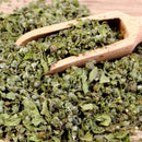 A wooden scoop rests on a pile of The Spice Lab Whole Marjoram leaves, ideal for bulk foodservice spice needs, scattered across a wooden surface.