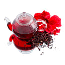 A glass teapot filled with red hibiscus tea sits beside The Spice Lab Whole Hibiscus Flowers, dried hibiscus petals, and a large red hibiscus flower from The Spice Lab, all arranged on a white background.