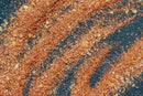 World Spice Buffalo Spice by World Spice, with its reddish-orange seasoning powder featuring fine grains and small yellow flakes, is scattered and swirled across a dark textured surface.