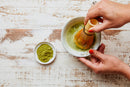 A person whisks World Spice Culinary Matcha, a vibrant green tea powder by World Spice, in a bowl with a bamboo whisk. A small dish of finely milled World Spice matcha sits nearby on a rustic wooden surface.