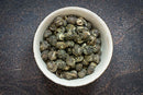 A white bowl filled with World Spice Jasmine Pearl tea pearls from World Spice rests on a dark, textured surface, inviting you to enjoy an aromatic tea experience.