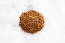 A small pile of World Spice Advieh, a finely ground brown Persian spice blend from World Spice, is spread on a white surface.