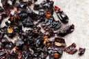 Close-up of World Spice Ancho Chile Flake by World Spice, showcasing chopped, dried dark red chile peppers commonly used in enchilada sauce or mole, scattered on a light-colored textured surface.