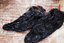Two dried, wrinkled World Spice Ancho Chiles with brown stems rest on a rustic, lightly colored wooden surface—perfect for infusing rich flavor into a classic Mexican mole.