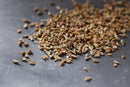 A close-up of World Spice Anise Seed by World Spice, scattered on a gray surface—these sweetly aromatic seeds are often used to flavor Italian pastries such as biscotti.