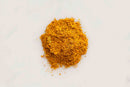 A small pile of World Spice Indonesian Ayam, a bright yellow-orange powder from World Spice resembling an Indonesian Ayam Goreng spice blend, sits on a plain white background.