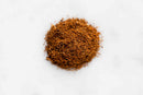 A small pile of finely ground brown World Spice Baharat from World Spice sits on a white surface, viewed from above.