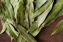 A close-up of several World Spice California Bay Leaf by World Spice, renowned for their intense flavor and aromatic camphor notes, scattered on a dark wooden surface.