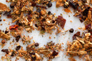 A close-up of World Spice Fin & Feather BBQ Rub by World Spice, scattered on a white surface, showcasing an enticing mix of dried spices and herbs with varied textures and vibrant shades of red, brown, and green.