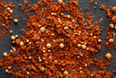 A close-up of World Spice Memphis Beale St. BBQ Rub by World Spice—featuring a vibrant blend of ground and whole spices, such as coriander seeds and red chili powder, scattered on a dark surface—ideal for crafting an authentic barbecue rub or perfectly seasoning pork shoulder for classic Memphis-style barbecue.