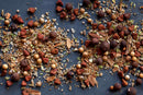 A close-up of a mix of dried spices—including coriander seeds, peppercorns, dried herbs, and bark pieces—scattered on a dark surface; these are key ingredients in the World Spice Yucatan Rojo BBQ Rub by World Spice, a traditional seasoning blend inspired by Mexican flavors.