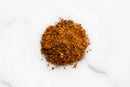 A small pile of World Spice Yucatan Rojo BBQ Rub, a reddish-brown ground spice mix from World Spice, rests on a white marble surface.