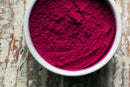A white bowl filled with bright magenta World Spice Beet Powder, a popular natural food coloring and baking ingredient from World Spice, sits on a rustic, weathered wooden surface.