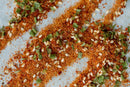 Close-up of World Spice Bulgogi Spice by World Spice scattered on a surface, showcasing its blend of orange gochugaru chili powder, white sesame seeds, and small green herbs.