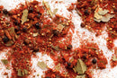 A close-up view of World Spice Cajun Black by World Spice, featuring a vibrant mix of dried herbs and spices—including black peppercorns, bay leaves, red paprika powder, and Cajun-inspired seasonings—scattered across a white surface.