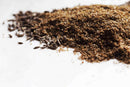 A close-up of World Spice Caraway Seed—ground and whole—scattered on a white surface, highlighting this essential World Spice ingredient often featured in Eastern European dishes like rye bread.