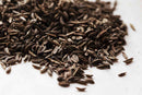 A pile of World Spice Caraway Seed from World Spice, known for its prominent use in Eastern European cuisine and the distinctive flavor it brings to classic rye bread, is scattered across a white surface.
