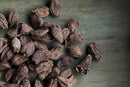 A cluster of World Spice Black Cardamom Pods from World Spice, an exotic spice celebrated for its smoky flavor, is scattered on a rustic, greenish wooden surface.