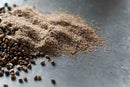 A close-up of World Spice Cardamom Seed by World Spice, featuring a pile of ground spices with whole seeds and freshly ground cardamom scattered on a metallic surface.