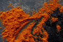 World Spice African Cayenne, a vibrant orange-red spice powder from World Spice, is scattered on a dark, textured surface, evoking the bold flavors often featured in Cajun dishes.