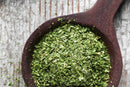 A wooden spoon filled with World Spice Chervil—dried, chopped green herbs from World Spice—rests on a rustic, weathered gray wooden surface.