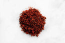 A small mound of World Spice Ancho Chili Powder, known for its mild heat, rests on a white surface.