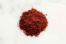 A small mound of World Spice Chipotle Chili Powder by World Spice, finely ground and reddish-brown in color, rests on a white marble surface.