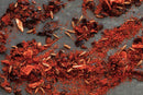 World Spice Chipotle Chili Powder by World Spice, along with red chili flakes and cumin seeds, are scattered across a dark gray surface.