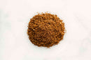A small pile of World Spice Chinese Five Spice, a finely ground brown spice blend from the brand World Spice, rests on a plain white background.