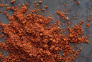 A pile of reddish-brown World Spice Chorizo Bomb, by World Spice, is scattered on a dark gray surface, promising a bold flavor punch reminiscent of authentic Mexican chorizo seasoning.