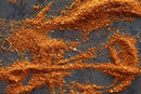 World Spice Cinnamon Toast Spice by World Spice—an orange-brown blend with rich hints of nutmeg and cinnamon—scattered on a dark surface, creating abstract patterns and textures.