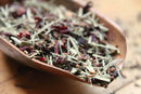 World Spice Copper Lemon loose herbal tea blend, featuring dried rooibos leaves and lemon hibiscus flower petals, from World Spice, displayed in a wooden scoop on a wooden surface.