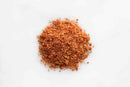 A small pile of reddish-brown World Spice Creole Spice by World Spice is scattered on a white background. The seasoning features visible flecks of herbs and ground spices, suggesting its signature peppery heat.