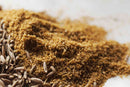 A close-up of World Spice Cumin Seed by World Spice, featuring whole cumin seeds and their finely ground powder on a white surface, highlighting the texture and color contrast between the whole seed spice and its milled form.