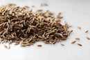 A close-up of World Spice Cumin Seed by World Spice, a popular seed spice, scattered across a white surface.