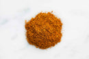A small mound of finely ground, orange-brown World Spice South African Curry—reminiscent of a classic South African curry blend from World Spice—rests on a white surface.