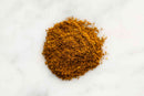 A small mound of World Spice Caribbean Curry, a golden-brown spice blend from World Spice with a rich hint of allspice, is spread on a white marble surface.