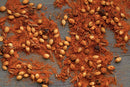 World Spice Tandoori Curry by World Spice, with its whole coriander seeds and reddish-brown ground spices reminiscent of classic Indian seasoning, is artfully scattered across a rustic wooden surface, creating a textured and colorful pattern.