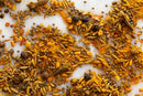 A close-up of assorted Indian spices scattered on a white surface—including turmeric powder, cumin seeds, coriander seeds, mustard seeds, peppercorns, and dried chili pieces—captures the essential ingredients found in World Spice Vadouvan Curry by World Spice, a blend inspired by the aromatic bases of mild curries in Puducherry’s renowned French-Indian cuisine.