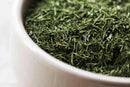 Close-up of a white bowl filled with World Spice Dill Weed by World Spice, displaying fine, thin, needle-like leaves and capturing the essence of their herbaceous flavor.