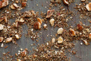 Crushed nuts and seeds, finely chopped and scattered across a gray wooden surface, evoke the rich textures and earthy brown tones of World Spice Hazelnut Dukkah—a savory Egyptian spice blend from World Spice, perfect for dipping.