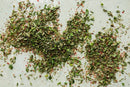 A scattered mix of World Spice Emerald City Seasoning by World Spice, featuring vibrant dried green herbs and red spices that evoke Pacific Northwest flavors, rests on a light, textured surface.
